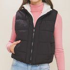 Woman wearing a black puffer vest over a pink sweater with a beige background