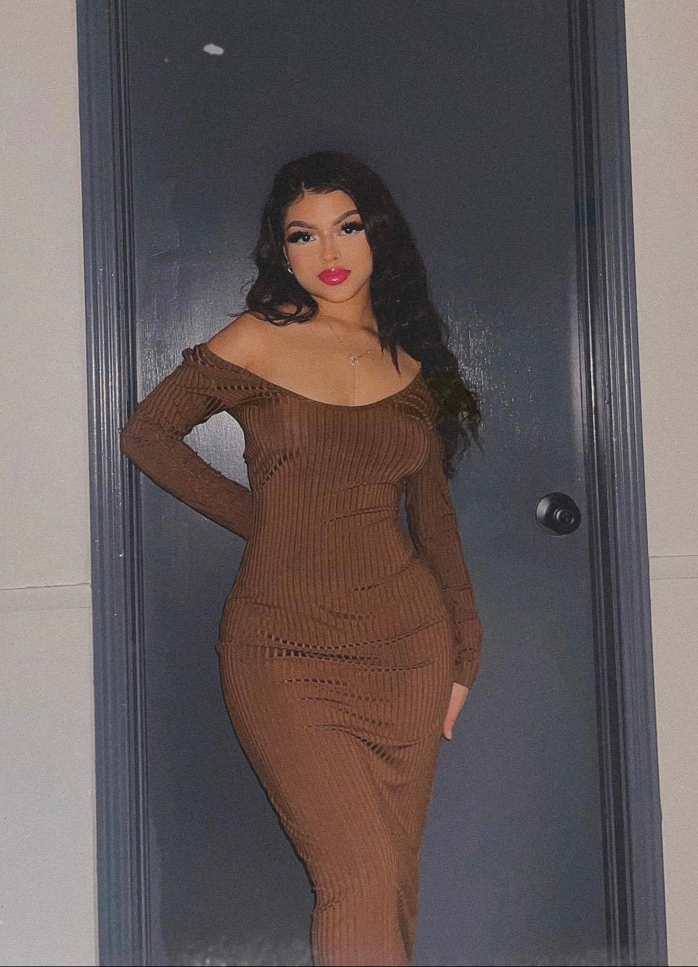 Woman in a brown dress standing in front of a dark door.