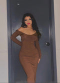Woman in a brown dress standing in front of a dark door.
