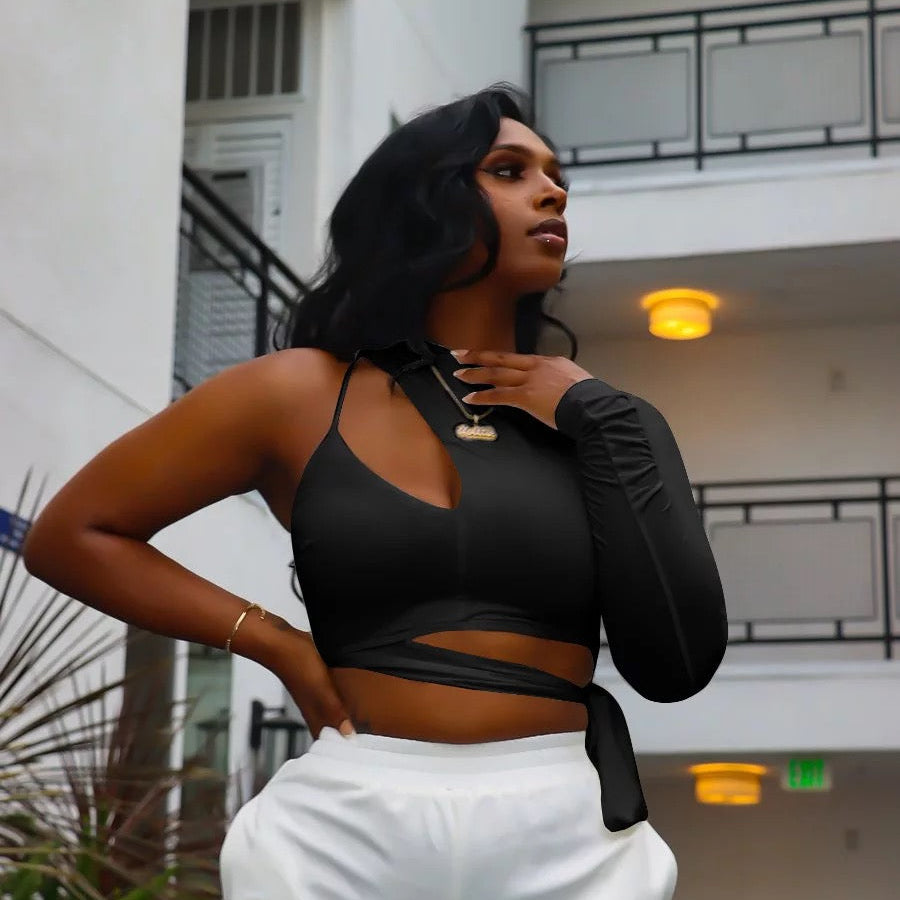 Woman in black one sleeve crop top and white sweat pants standing in front of a building.
