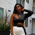 Woman in black one sleeve crop top and white sweat pants standing in front of a building.